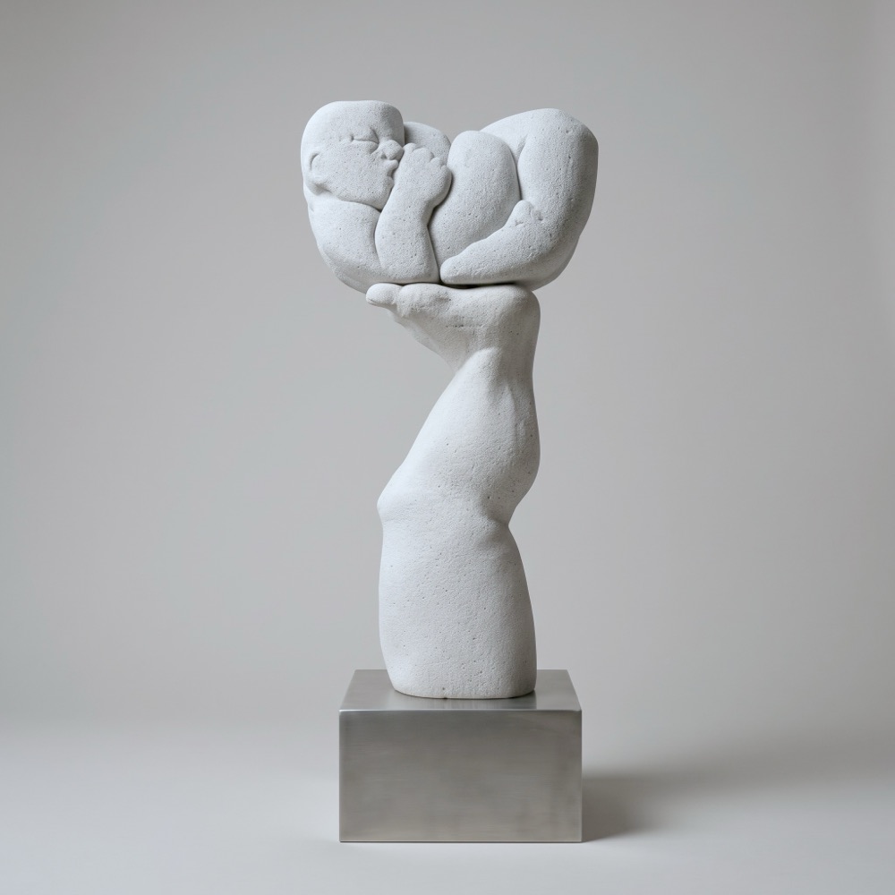 A single arm rises from a steel base; its upturned hand holds a curled, sleeping infant.