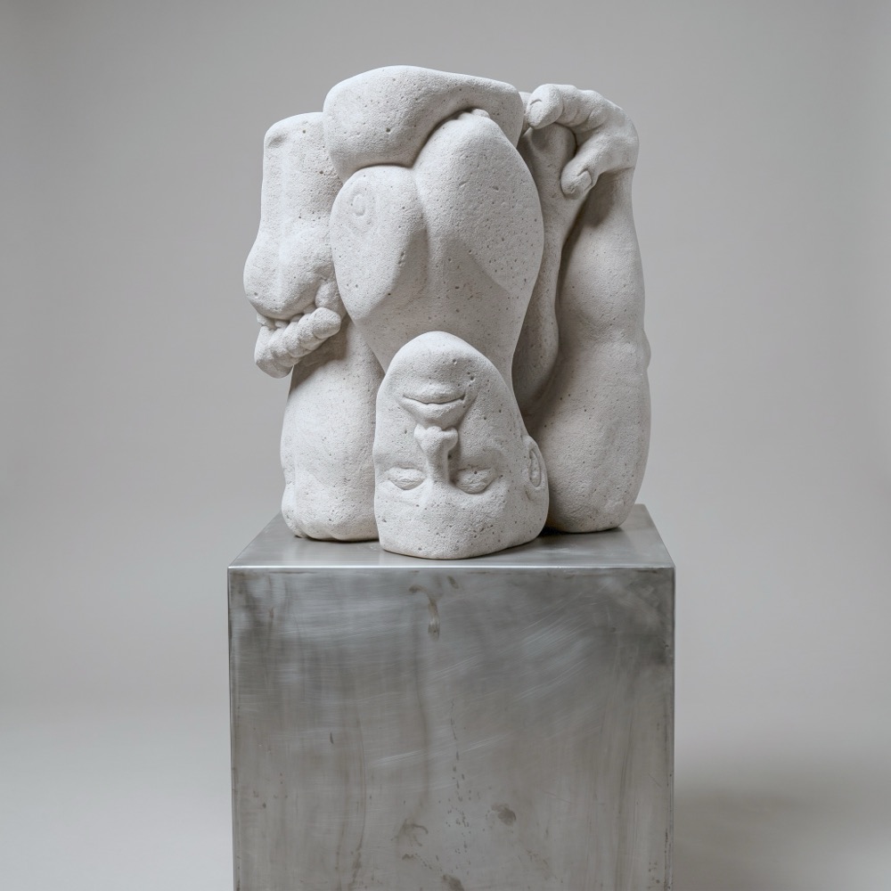 A block of pale aerated concrete on a tall dark steel pedestal. A single body is folded inside it: the head upside down at the base, a hand gripping the top edge.